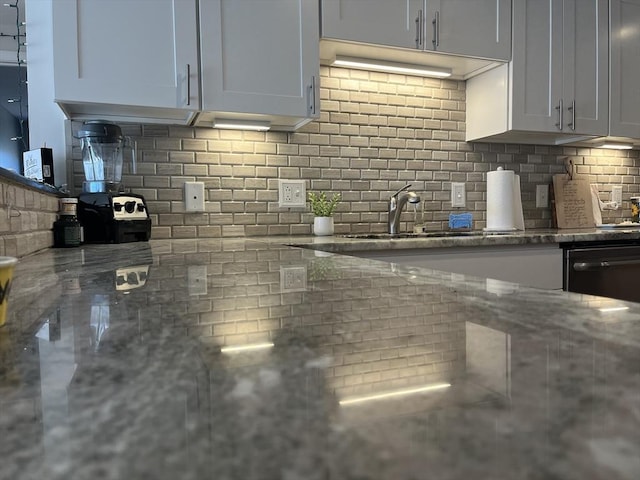kitchen featuring backsplash, a sink, light stone countertops, and black dishwasher