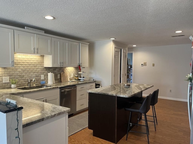 kitchen featuring dishwasher, a sink, decorative backsplash, recessed lighting, and wood finished floors