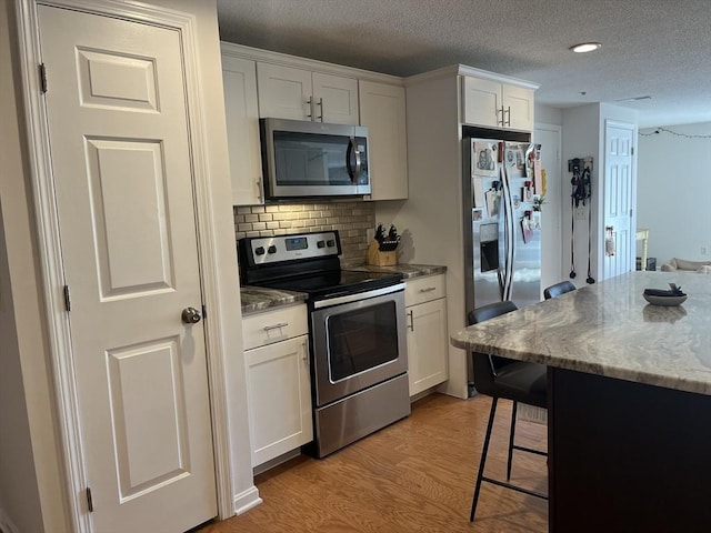 kitchen with stainless steel appliances, light wood-style floors, a kitchen breakfast bar, white cabinetry, and light stone counters