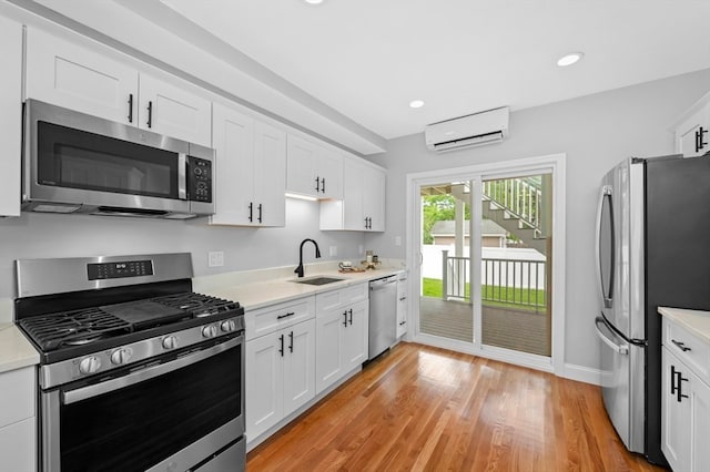 kitchen featuring appliances with stainless steel finishes, light hardwood / wood-style flooring, sink, white cabinets, and a wall mounted AC