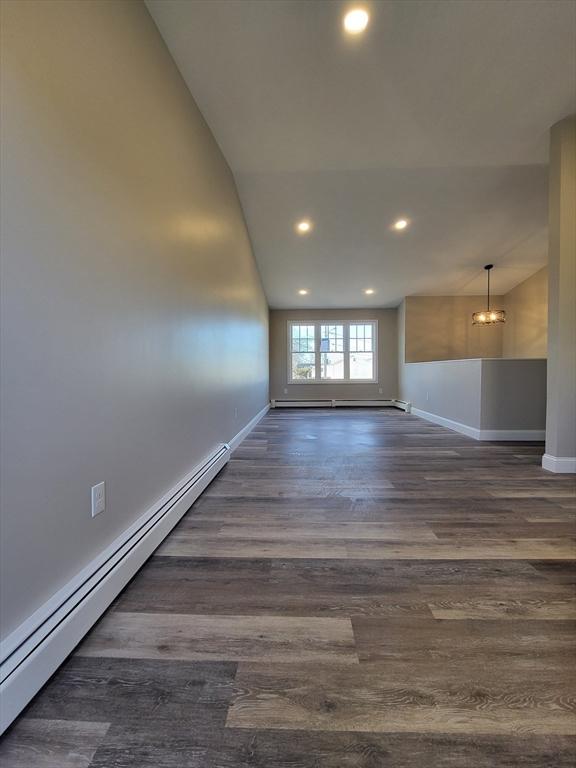 spare room with an inviting chandelier, dark hardwood / wood-style flooring, lofted ceiling, and a baseboard radiator