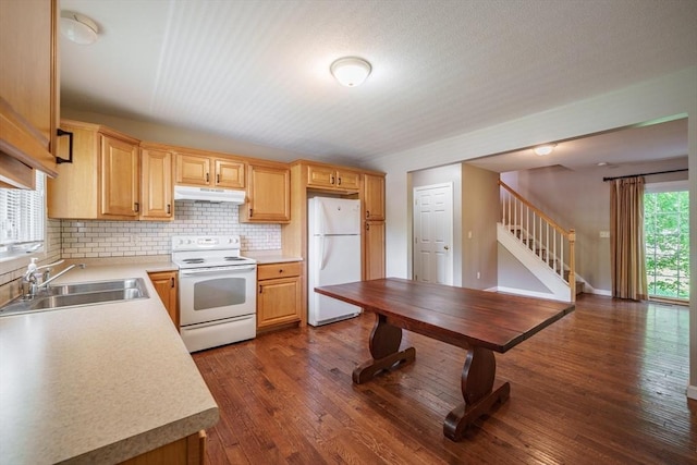 kitchen with white appliances, under cabinet range hood, a sink, tasteful backsplash, and dark wood-style flooring