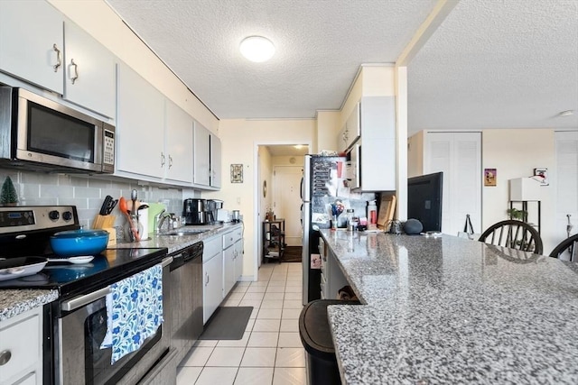 kitchen with light tile patterned floors, stainless steel appliances, tasteful backsplash, light stone countertops, and a textured ceiling