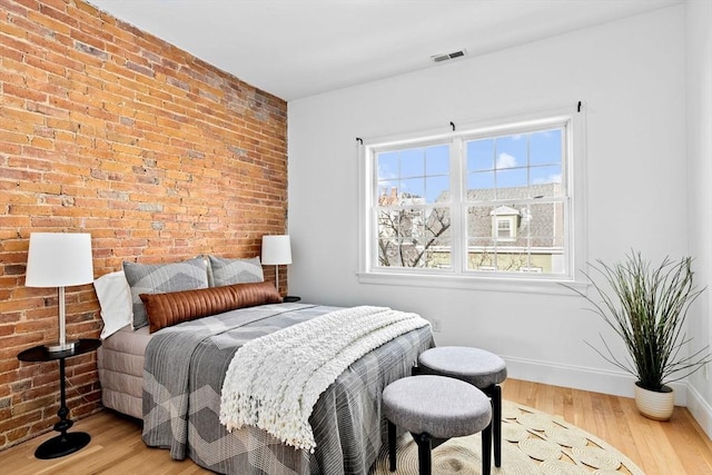 bedroom featuring brick wall, visible vents, baseboards, and wood finished floors