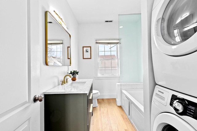 full bathroom featuring stacked washer and dryer, toilet, vanity, wood finished floors, and a tub