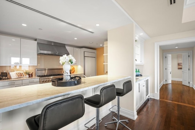 kitchen with light stone countertops, white cabinetry, a kitchen breakfast bar, wall chimney exhaust hood, and range