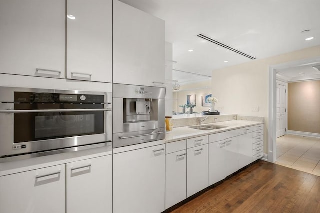 kitchen with a sink, oven, light countertops, white cabinetry, and dark wood-style flooring