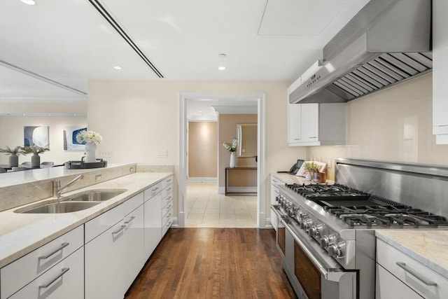 kitchen with light stone countertops, white cabinetry, a sink, high end stainless steel range oven, and wall chimney range hood