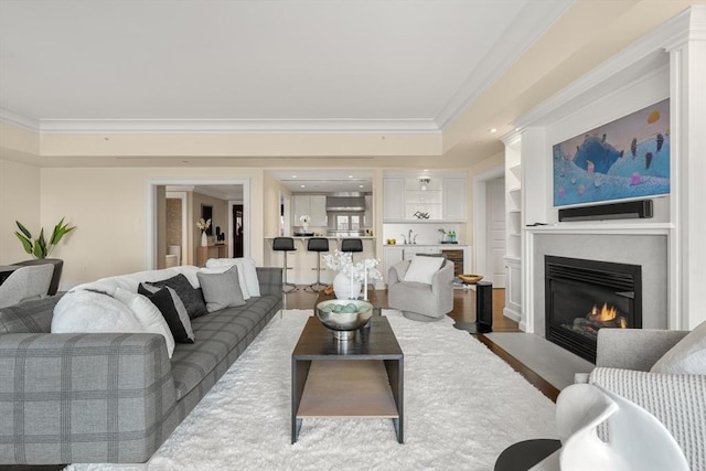 living room featuring a fireplace with flush hearth, a raised ceiling, crown molding, and wood finished floors