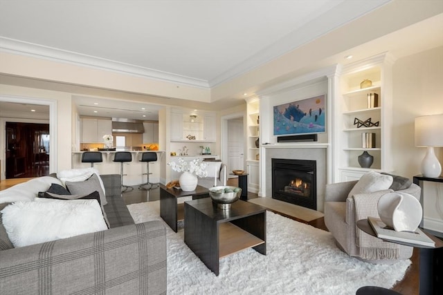 living area with wood finished floors, a fireplace with flush hearth, and ornamental molding