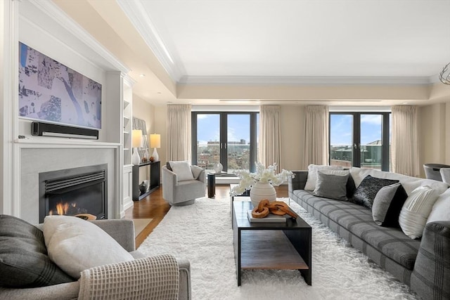 living area featuring french doors, plenty of natural light, a glass covered fireplace, and crown molding