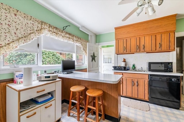 kitchen with ceiling fan, sink, a center island, a kitchen breakfast bar, and black appliances