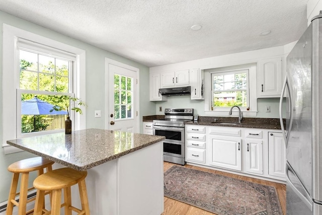 8 May St, Sharon, MA 02067 - kitchen with stainless steel appliances, under cabinet range hood, a textured ceiling, white cabinetry, and dark stone counters