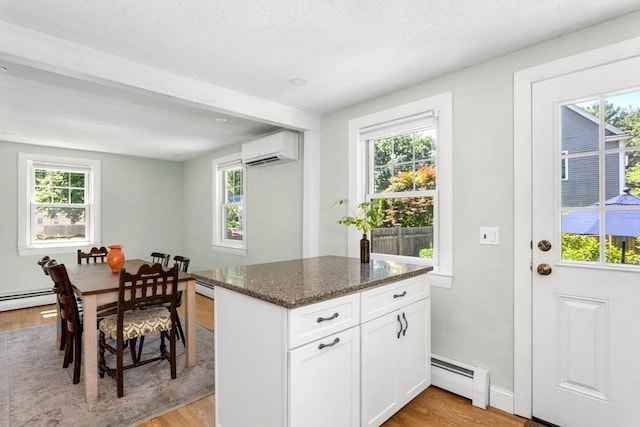 8 May St, Sharon, MA 02067 - kitchen featuring a baseboard heating unit, light wood finished floors, dark stone countertops, a wall mounted air conditioner, and a textured ceiling