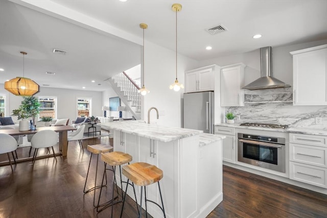 kitchen featuring hanging light fixtures, appliances with stainless steel finishes, white cabinets, and wall chimney exhaust hood