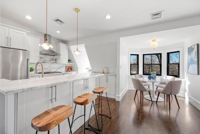 kitchen featuring wall chimney range hood, decorative light fixtures, decorative backsplash, and white cabinets