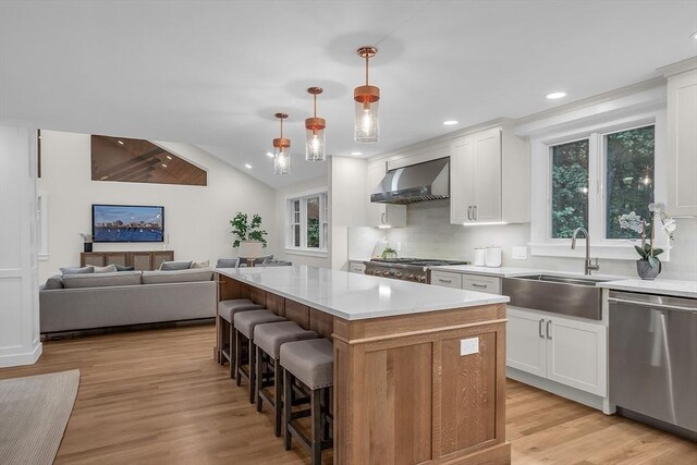 kitchen with a kitchen island, light wood-type flooring, white cabinetry, premium appliances, and wall chimney exhaust hood