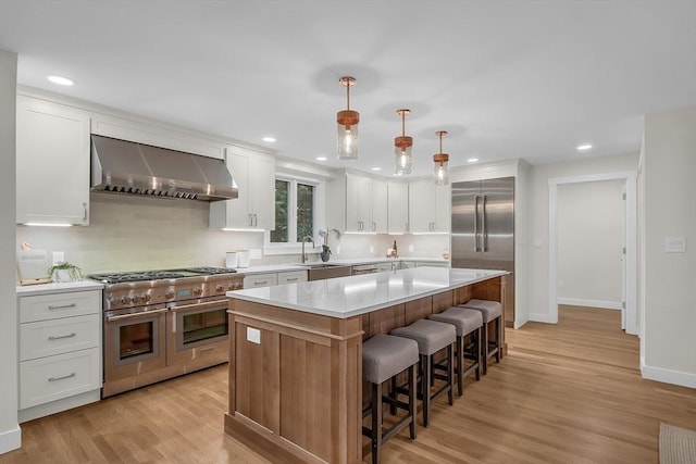 kitchen featuring wall chimney exhaust hood, high end appliances, a kitchen island, pendant lighting, and white cabinets