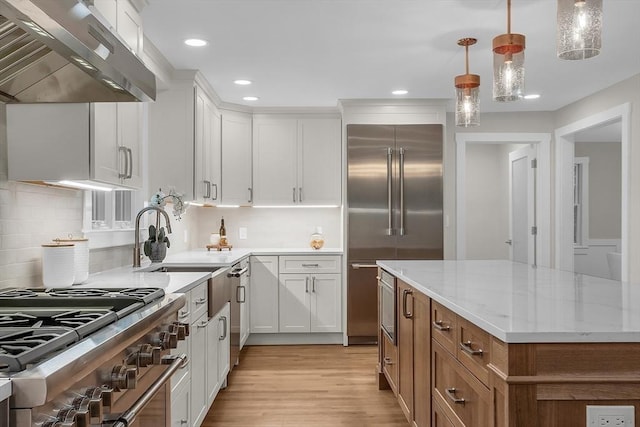 kitchen with white cabinetry, high quality appliances, light stone counters, ventilation hood, and decorative light fixtures