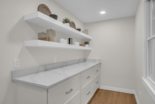 bar with white cabinetry, light stone countertops, and light hardwood / wood-style floors