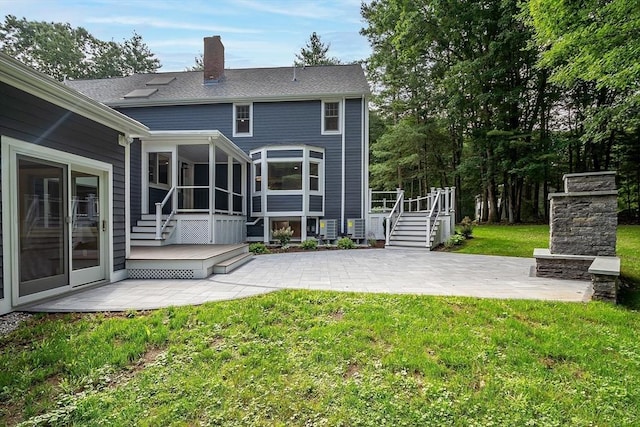 rear view of house with an outdoor stone fireplace, a yard, a patio, a wooden deck, and a sunroom