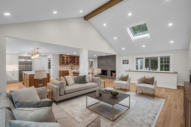 living room with a skylight, high vaulted ceiling, beam ceiling, and light hardwood / wood-style flooring