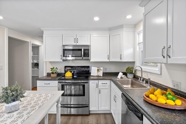 kitchen featuring dark countertops, appliances with stainless steel finishes, wood finished floors, white cabinets, and a sink