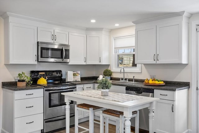 kitchen with a sink, a kitchen breakfast bar, recessed lighting, appliances with stainless steel finishes, and white cabinets