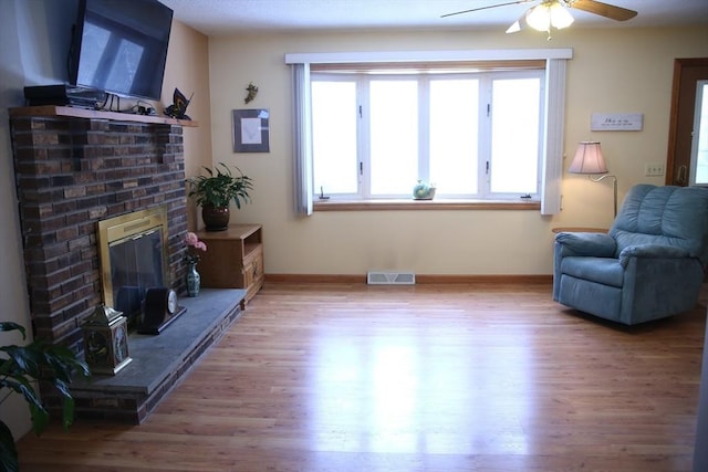 sitting room featuring a fireplace, ceiling fan, and light hardwood / wood-style floors