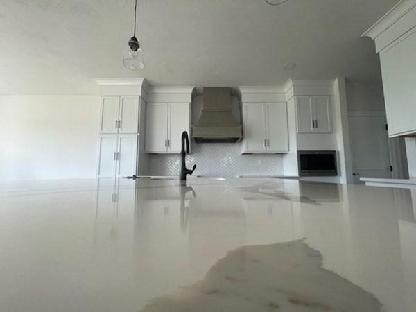 kitchen with wall chimney exhaust hood, decorative backsplash, white cabinetry, and hanging light fixtures