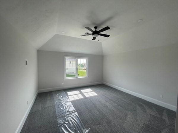 additional living space with dark colored carpet, ceiling fan, and vaulted ceiling