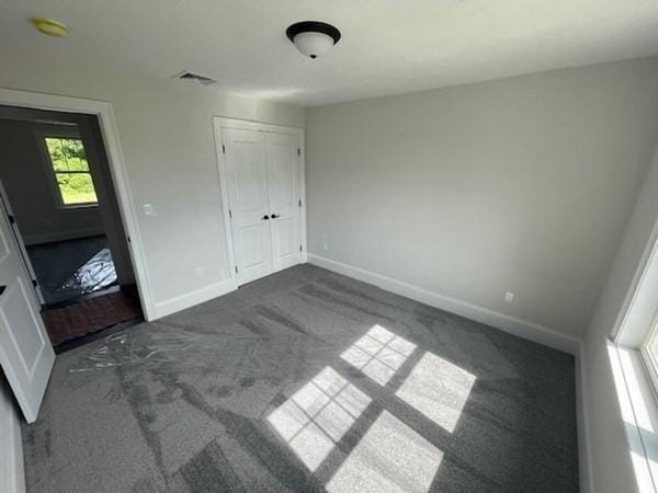 unfurnished bedroom featuring dark colored carpet, multiple windows, and a closet