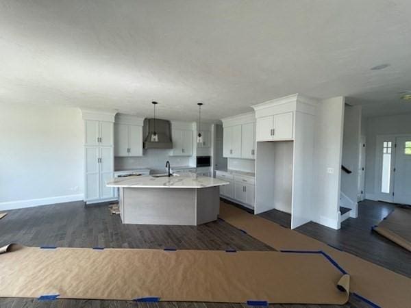 kitchen featuring white cabinetry, sink, hanging light fixtures, dark hardwood / wood-style floors, and a center island with sink