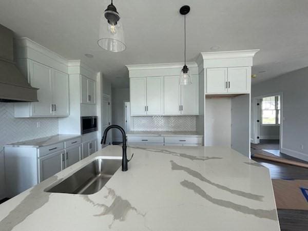 kitchen featuring white cabinetry, light stone countertops, sink, hanging light fixtures, and wall chimney range hood