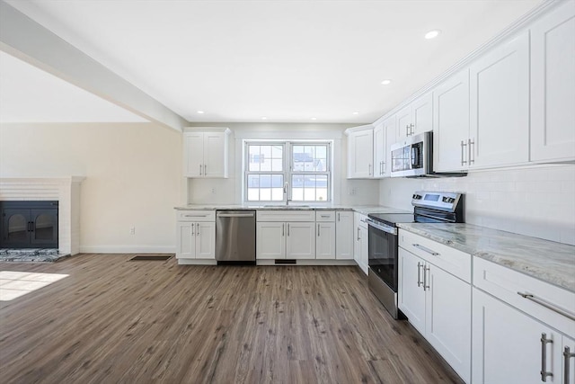 kitchen featuring sink, appliances with stainless steel finishes, white cabinetry, light stone countertops, and dark hardwood / wood-style flooring