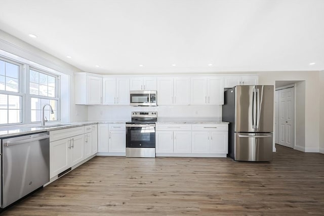 kitchen with white cabinetry, stainless steel appliances, sink, and hardwood / wood-style floors