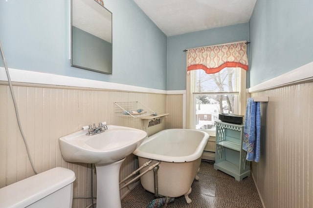 bathroom with baseboard heating, sink, toilet, a bathing tub, and wooden walls