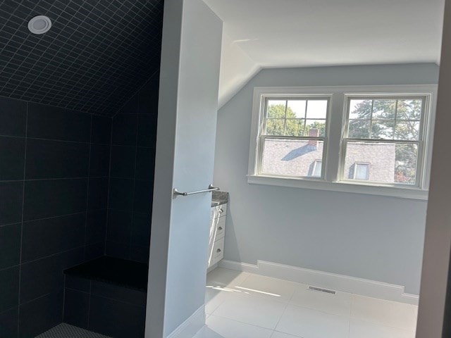 bathroom with vaulted ceiling, a tile shower, and tile patterned flooring