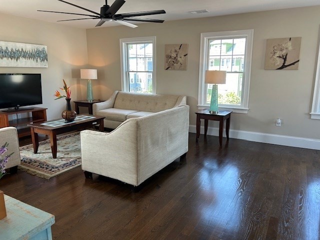 living room featuring dark wood-type flooring, ceiling fan, and a wealth of natural light