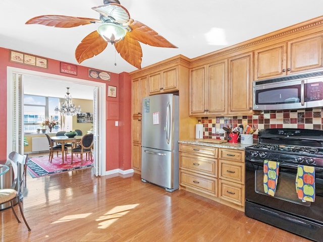 kitchen featuring light hardwood / wood-style flooring, ceiling fan with notable chandelier, stainless steel appliances, tasteful backsplash, and light stone countertops