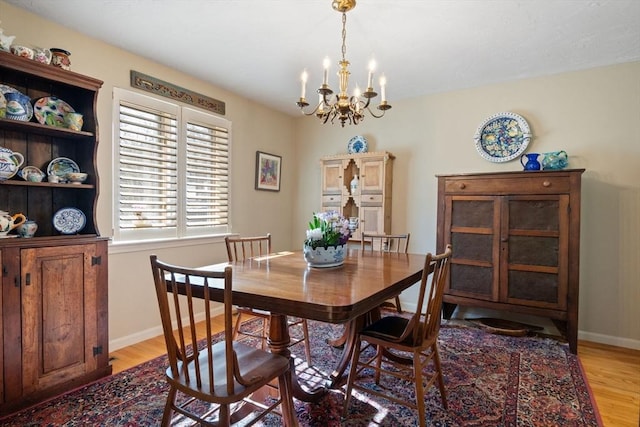 dining area with light wood-type flooring, baseboards, and a notable chandelier