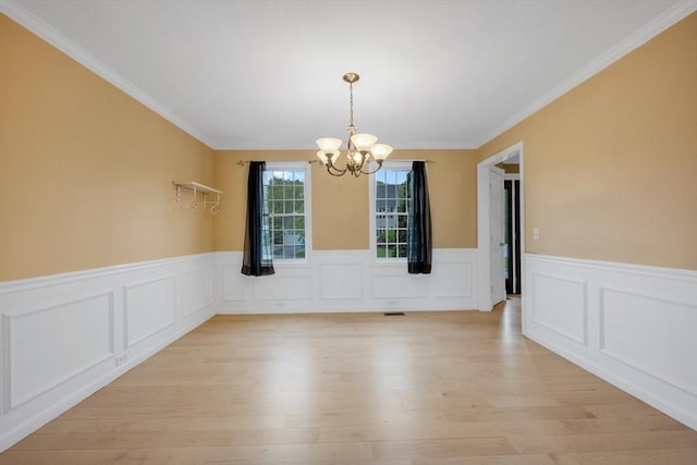 unfurnished dining area featuring a chandelier, a wainscoted wall, light wood-style flooring, and crown molding