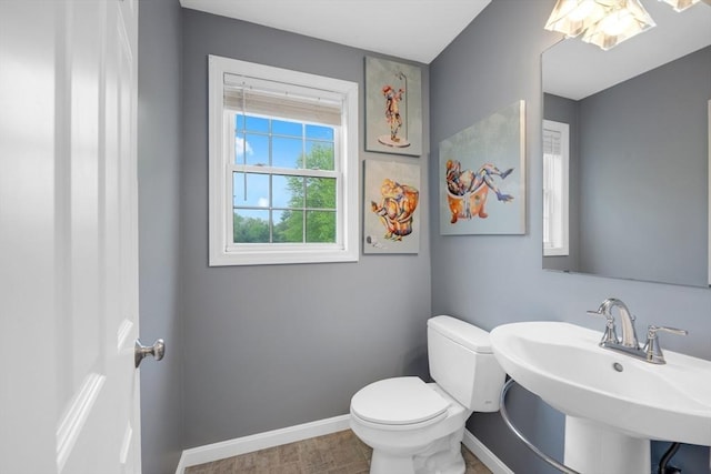 half bathroom with baseboards, toilet, and a sink