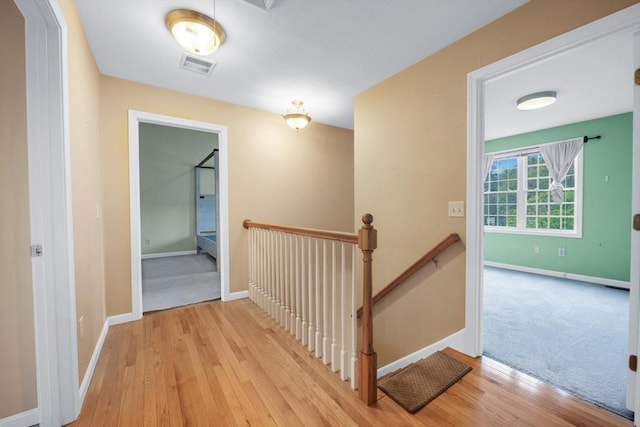 hallway with an upstairs landing, baseboards, and wood finished floors