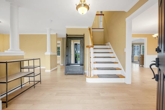 staircase with ornate columns, wood finished floors, ornamental molding, and baseboards