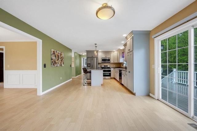 kitchen featuring appliances with stainless steel finishes, a kitchen bar, a sink, a kitchen island, and light wood finished floors
