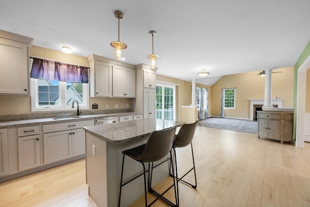 kitchen featuring a sink, light wood-style flooring, a kitchen island, lofted ceiling, and light stone countertops