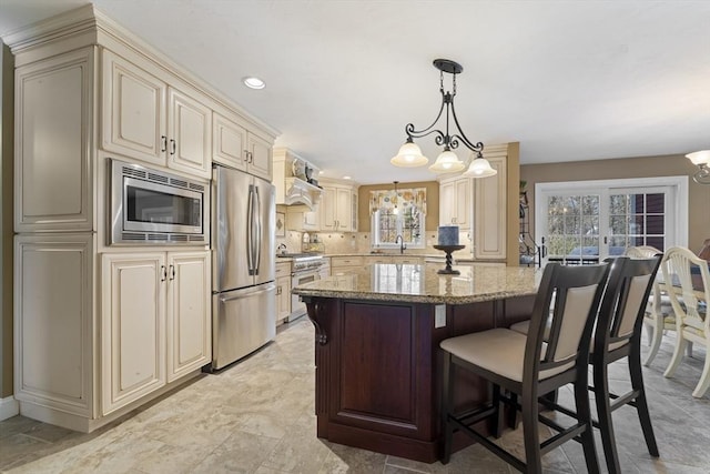 kitchen featuring an inviting chandelier, cream cabinets, light stone counters, stainless steel appliances, and a kitchen island