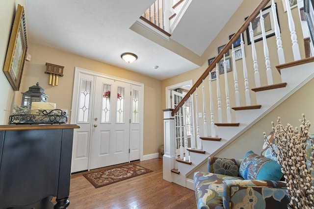 foyer entrance with stairs, wood finished floors, and baseboards