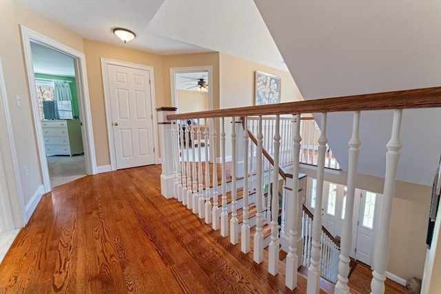 hall with baseboards, wood finished floors, and an upstairs landing